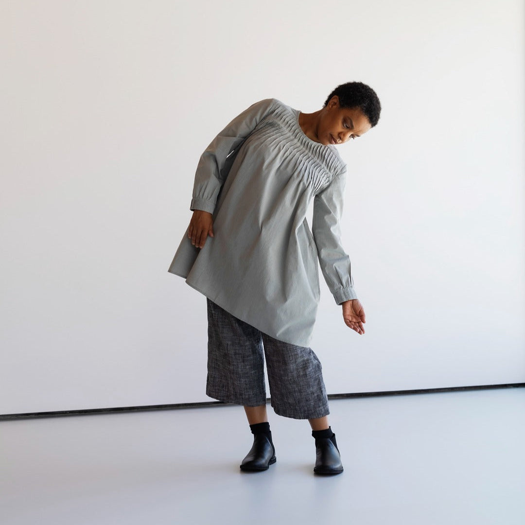 Person wearing a pleated ight gray dress against a white background