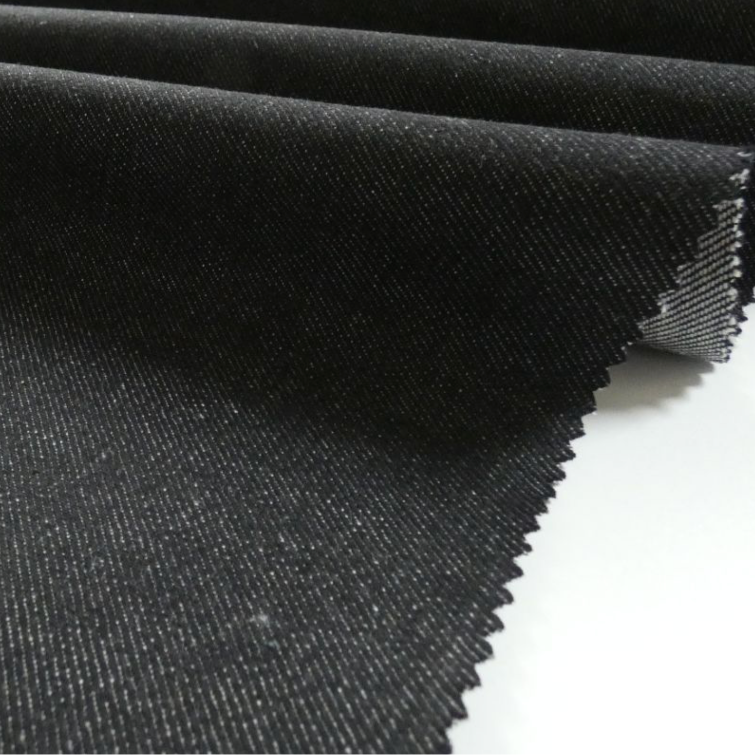 A close-up of folded black was denim with piked edges, placed on a white background.