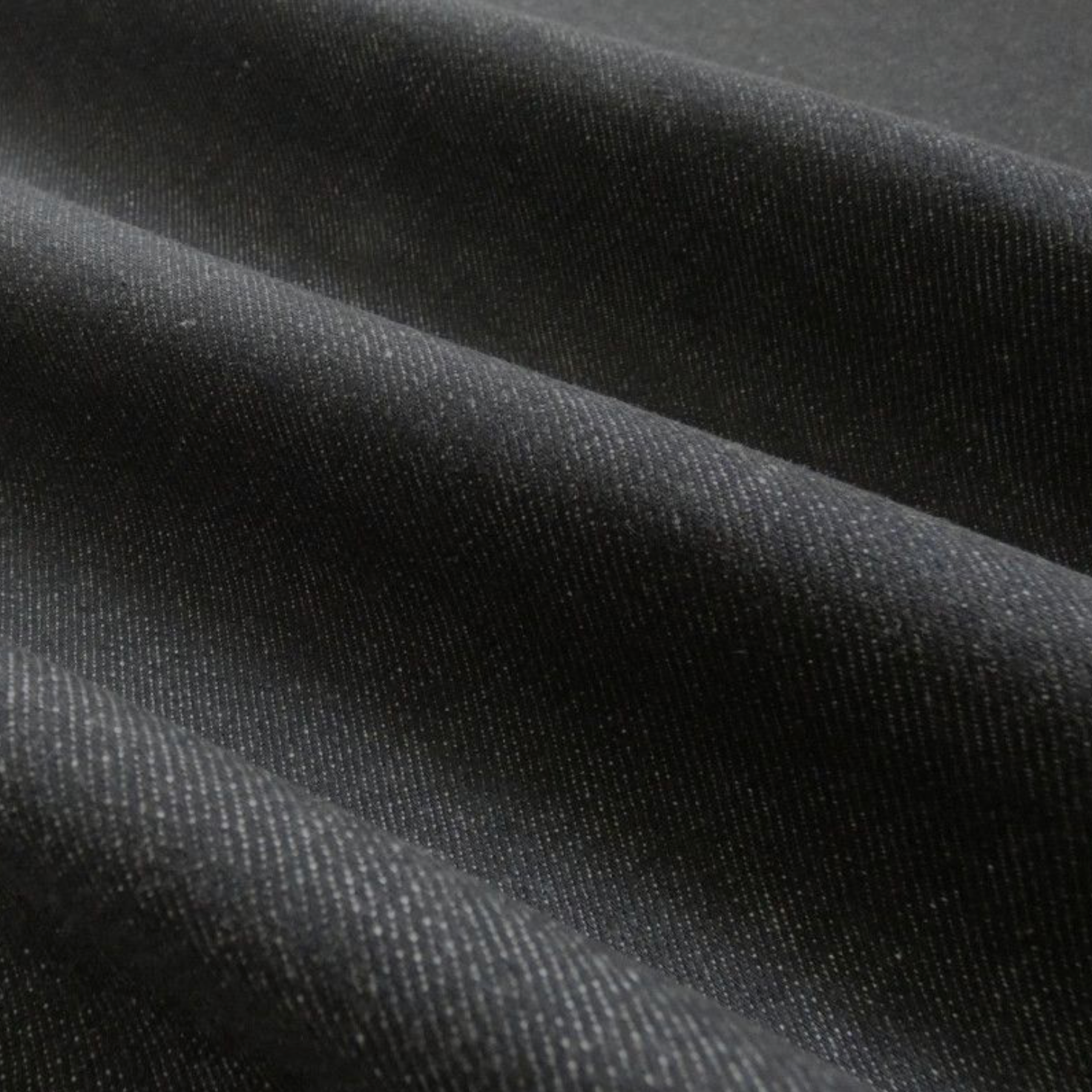A close-up of draped black denim, showing soft folds and shadows.