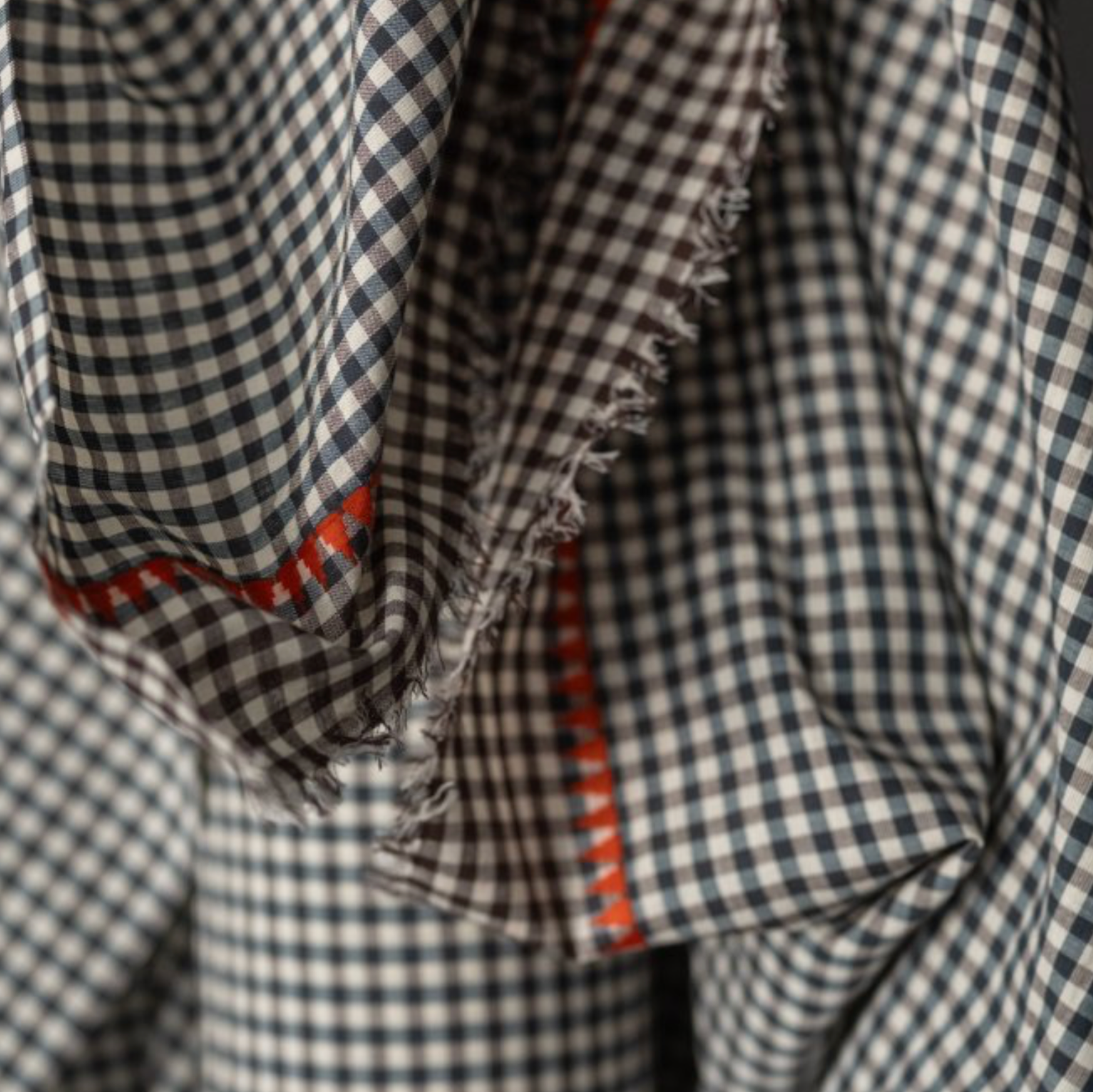 Close-up of a dark blue and white gingham check fabric with brown  gingham selvegde and a orange  embroidery running parallel to the selvedge.
