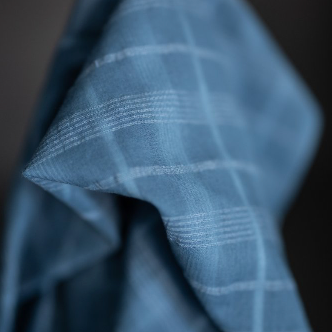A close-up of a blue plaid fabric, showing the texture and windowpane woven pattern.