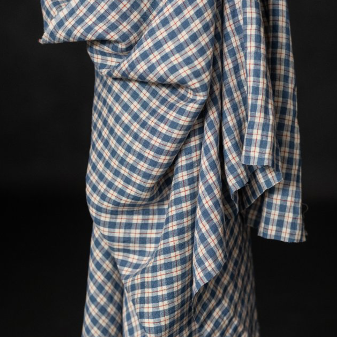 A close-up of a draped blue and beige plaid fabric, showing the texture and pattern against a solid black background.