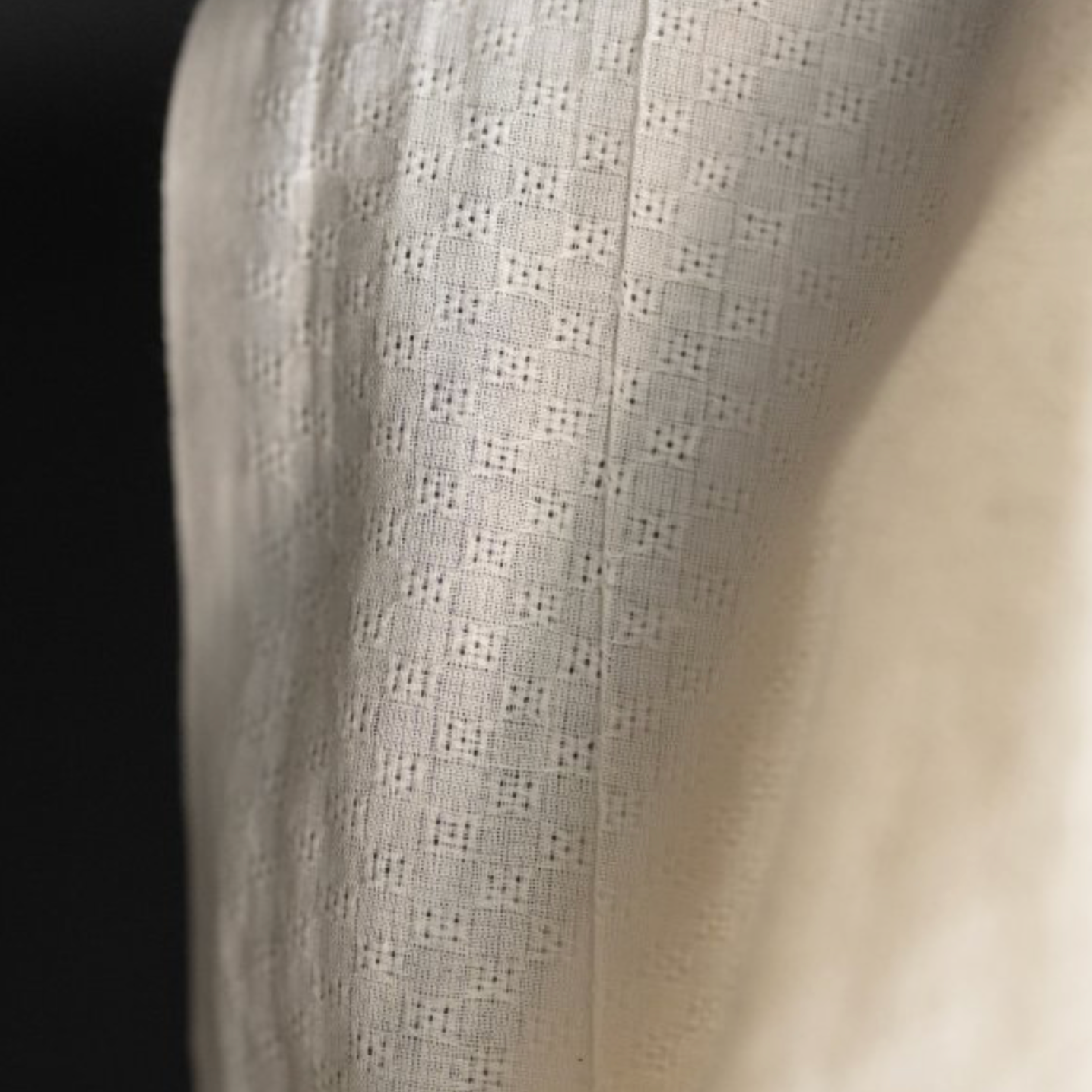 Close-up of sheer ecru textured fabric with a subtle woven geometric pattern.