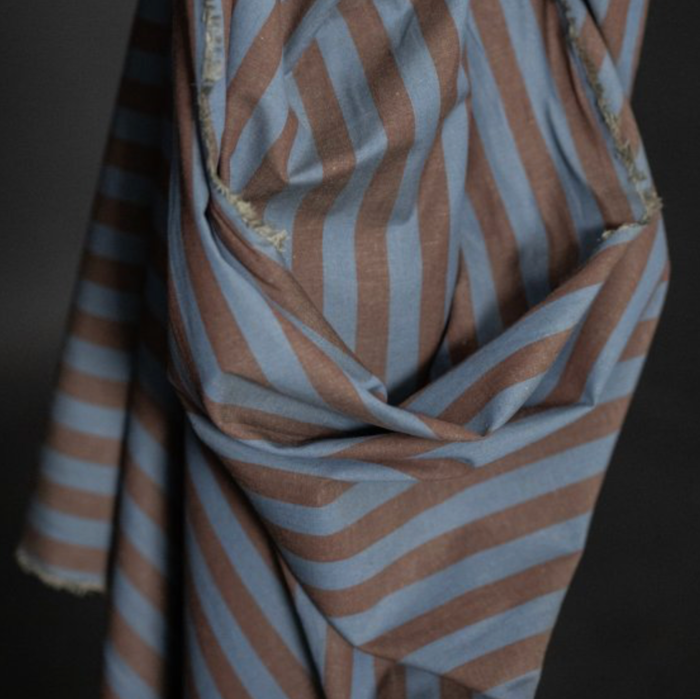 A close-up of draped striped fabric with alternating dusty blue and warm brown.