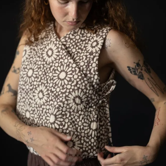 A woman with curly hair wearing a sleeveless wrap-style top.